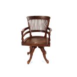 An early 20th Century mahogany slat back revolving desk chair, the shaped solid seat raised on