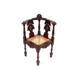 A carved mahogany corner chair, with profuse mask and foliate decoration, cane work seat raised on