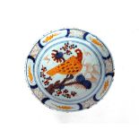 An English Delftware plate, painted with a large yellow stylised bird seated on a branch within blue