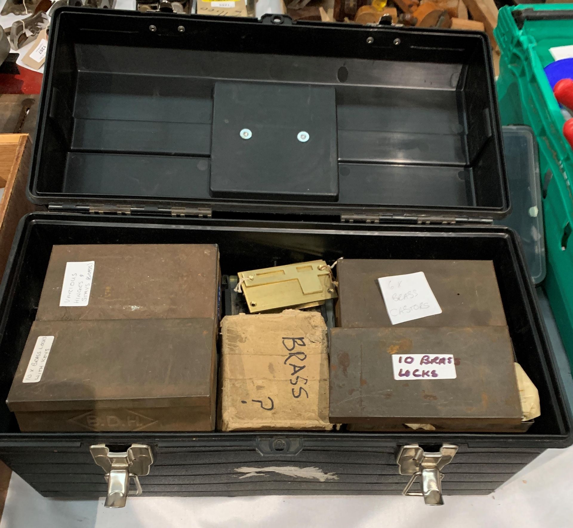 A black plastic tool box and contents - boxes of brass locks, brass hinges, castors,