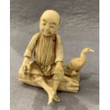 A late 19th/early 20th century ivory figure group of a man sat on a a log next to a cormorant,