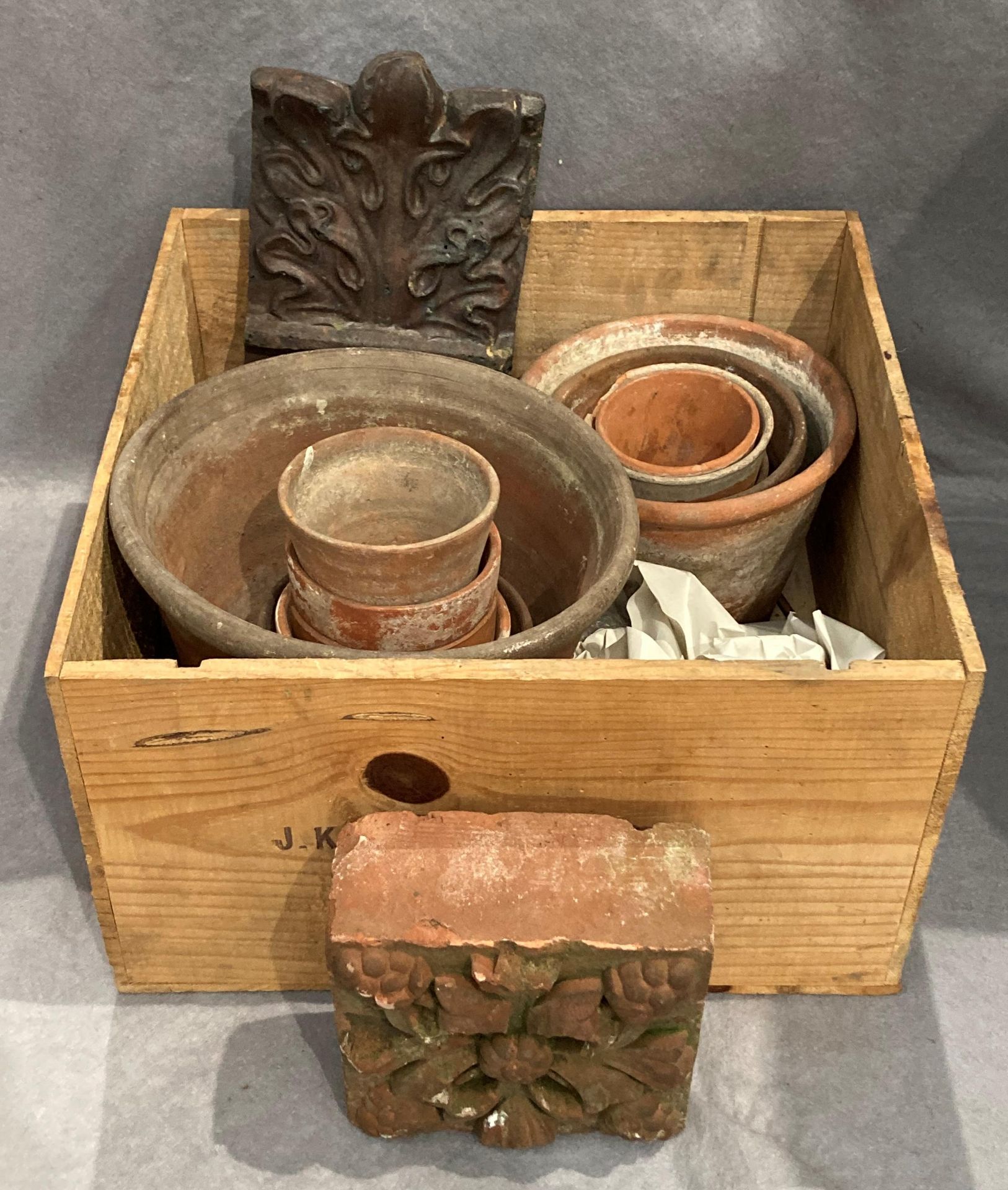 A small wood crate containing a small quantity of assorted sized terracotta plant pots,