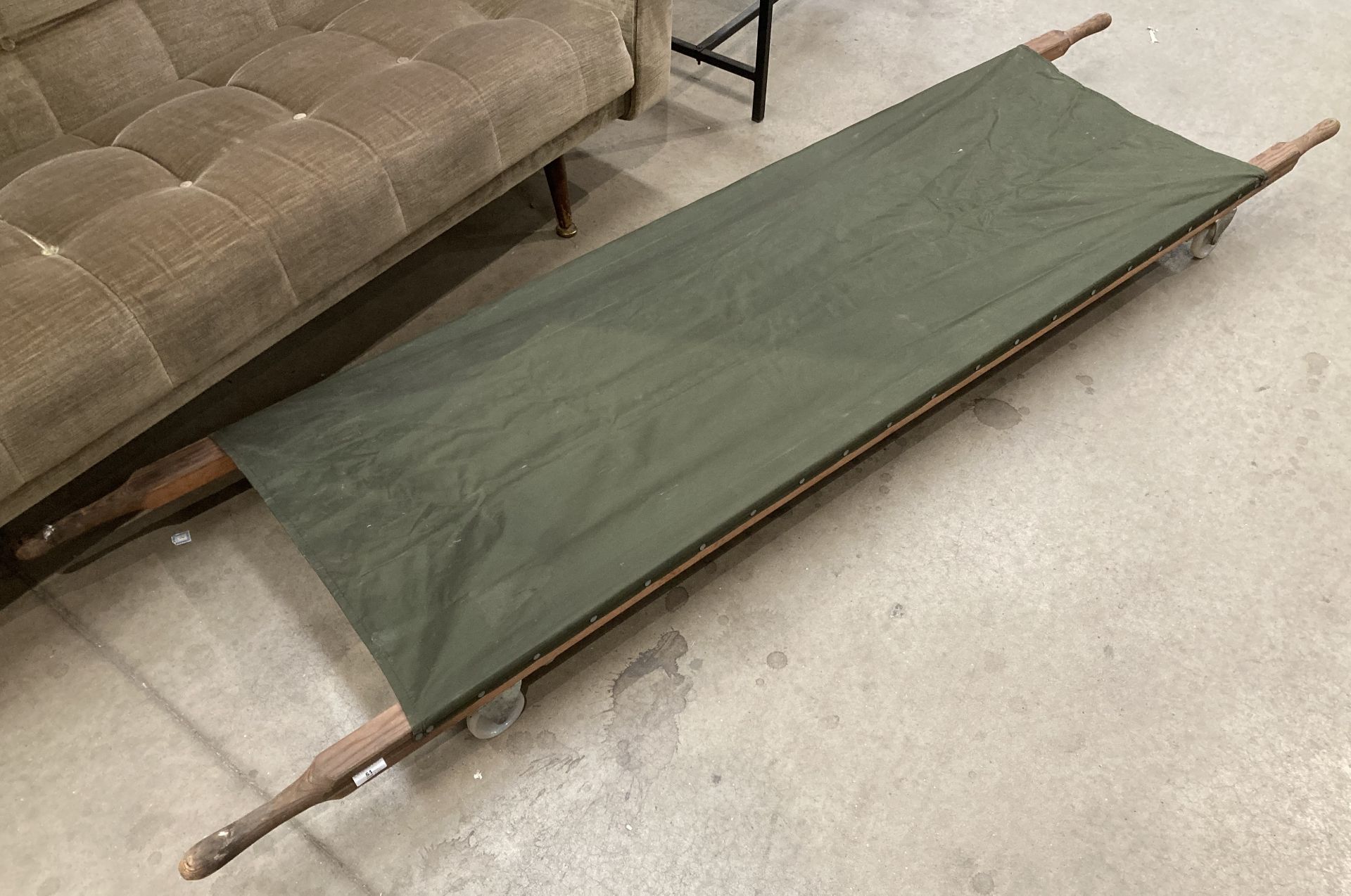 A wood framed military stretcher 230cm x 60cm when open fitted with castors and green fabric