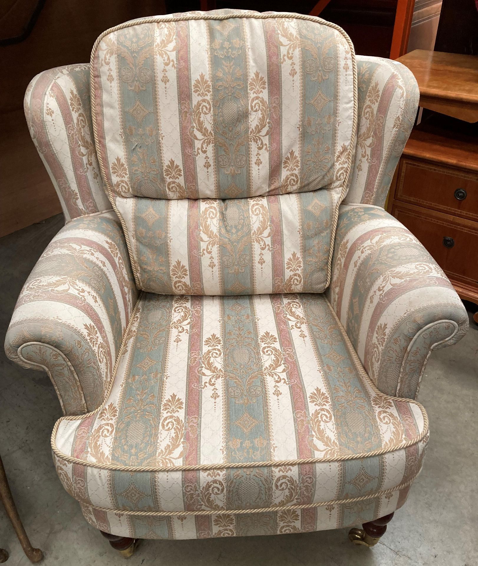 A green/gold and white patterned wing back lounge armchair on brass castors (complete with fire