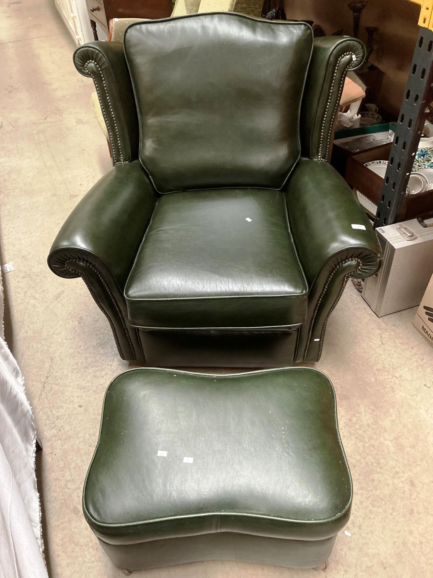 A dark green leather wing back armchair with matching pouffe - please note no fire certificates,