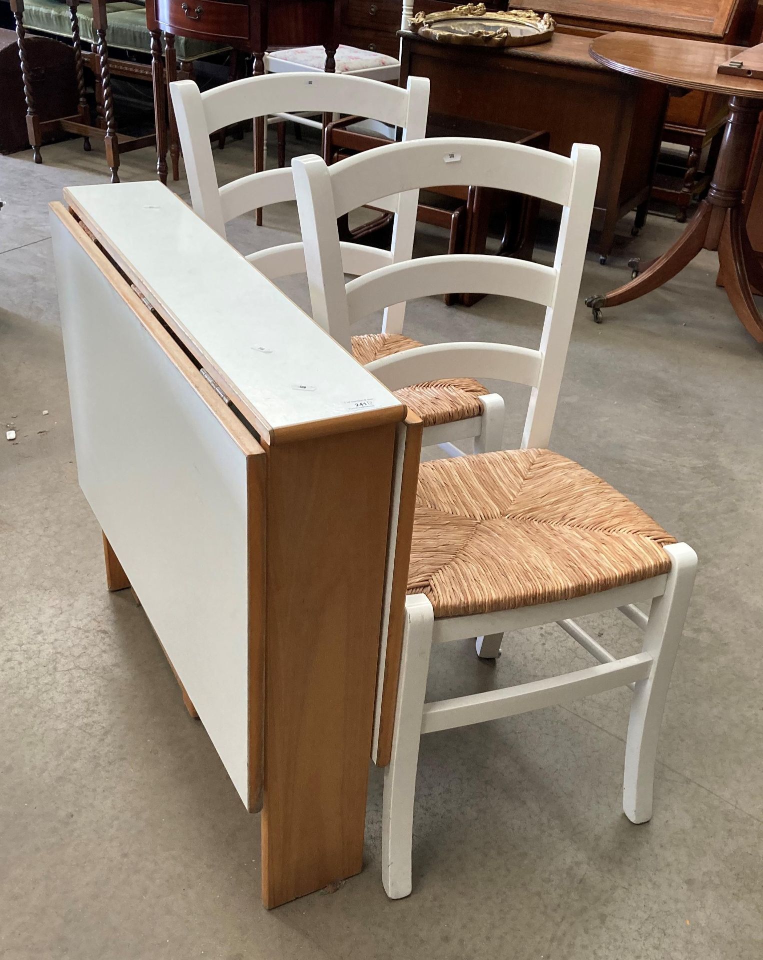 A white melamine drop leaf table 80 x 115cm when open and two white painted chairs with woven seats