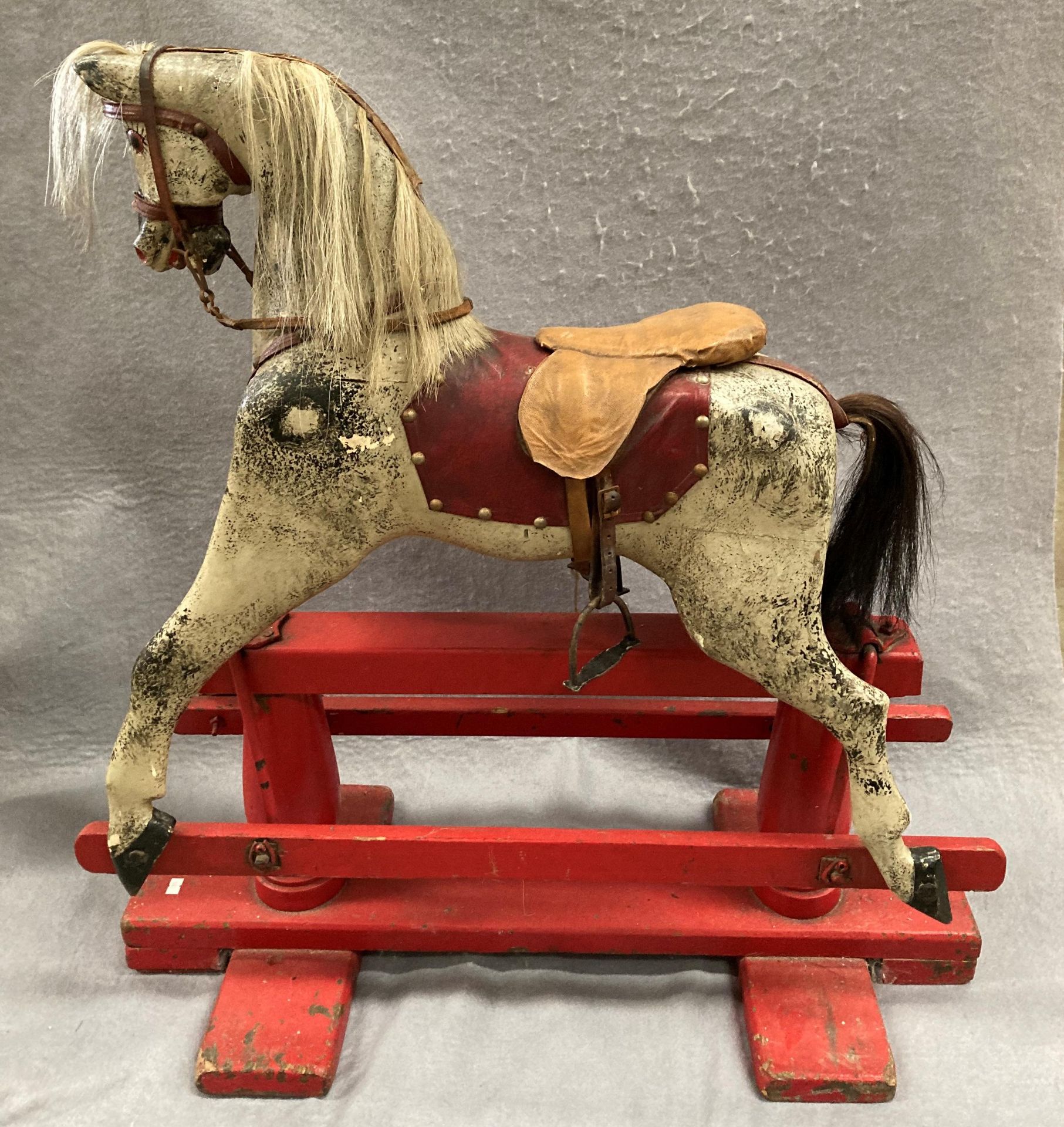 An old dapple grey composition rocking horse on red painted wooden frame, length approximately 80cm,