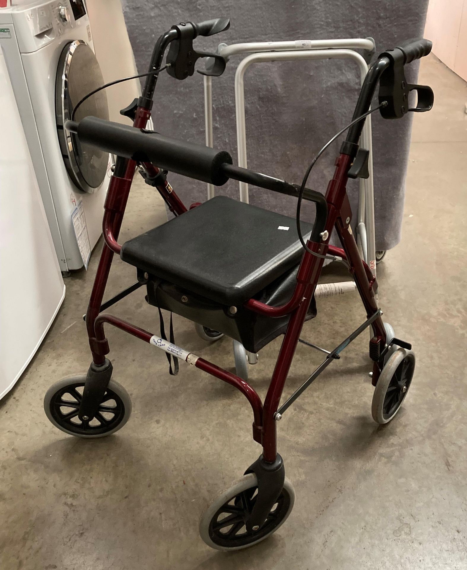 A red metal four wheel mobility walking aid and a grey metal two wheel mobility walking aid (2)