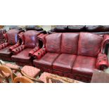 An oxblood leather upholstered wingback three piece suite comprising three seater settee and two