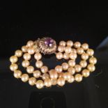 A triple strand simulated pearl bracelet set with flower design 9ct gold clasp with amethyst centre
