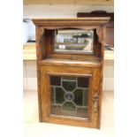 An Edwardian oak wall cabinet with mirror back and stained glass door panel