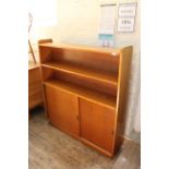 A mid Century teak bookcase with two shelves above two sliding door cupboards