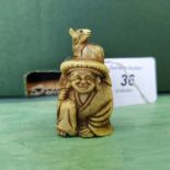 An antique detailed carved ivory netsuke of a seated figure with a rat on his head,