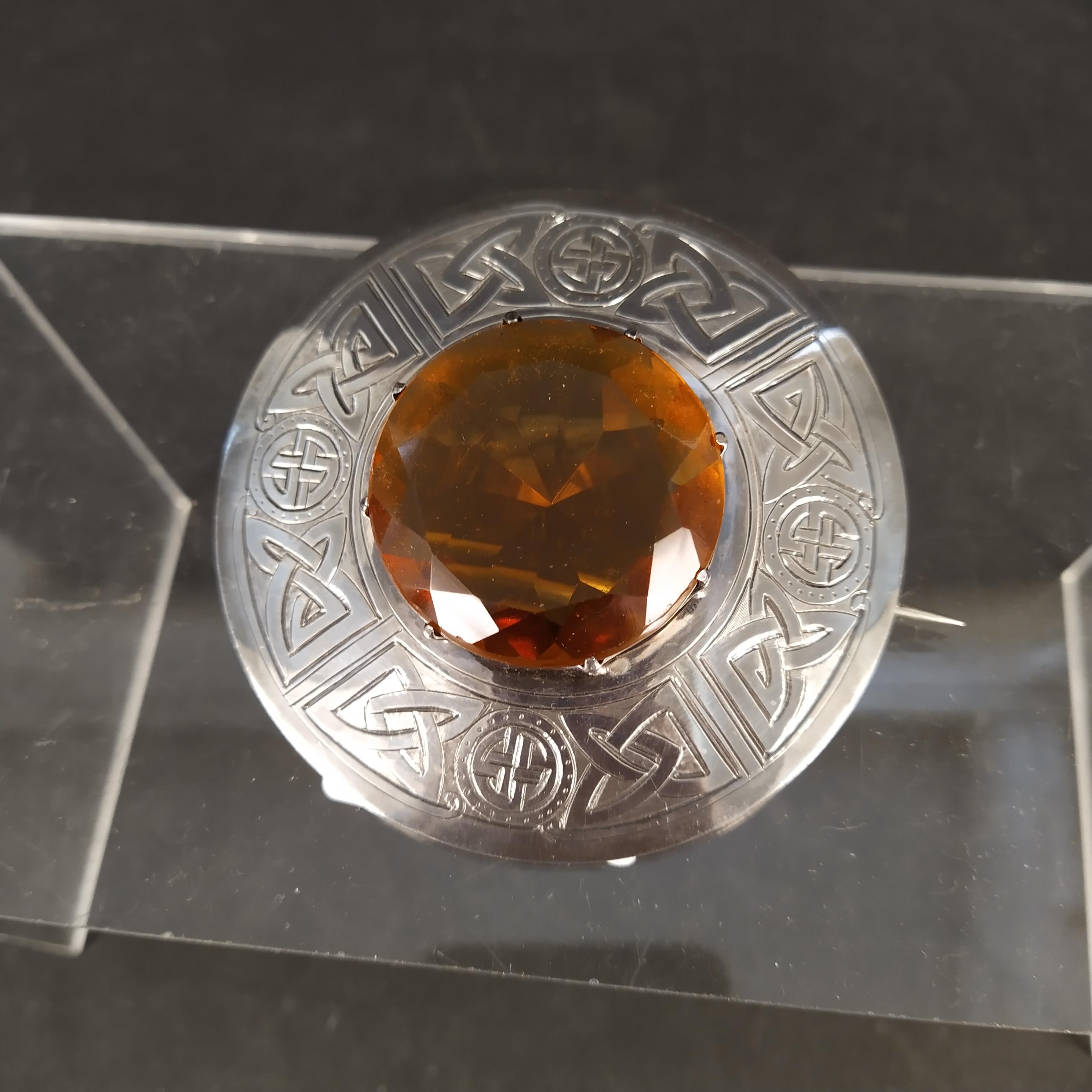 A Scottish silver plaid brooch with engraved Celtic design surrounding a large central orange stone,