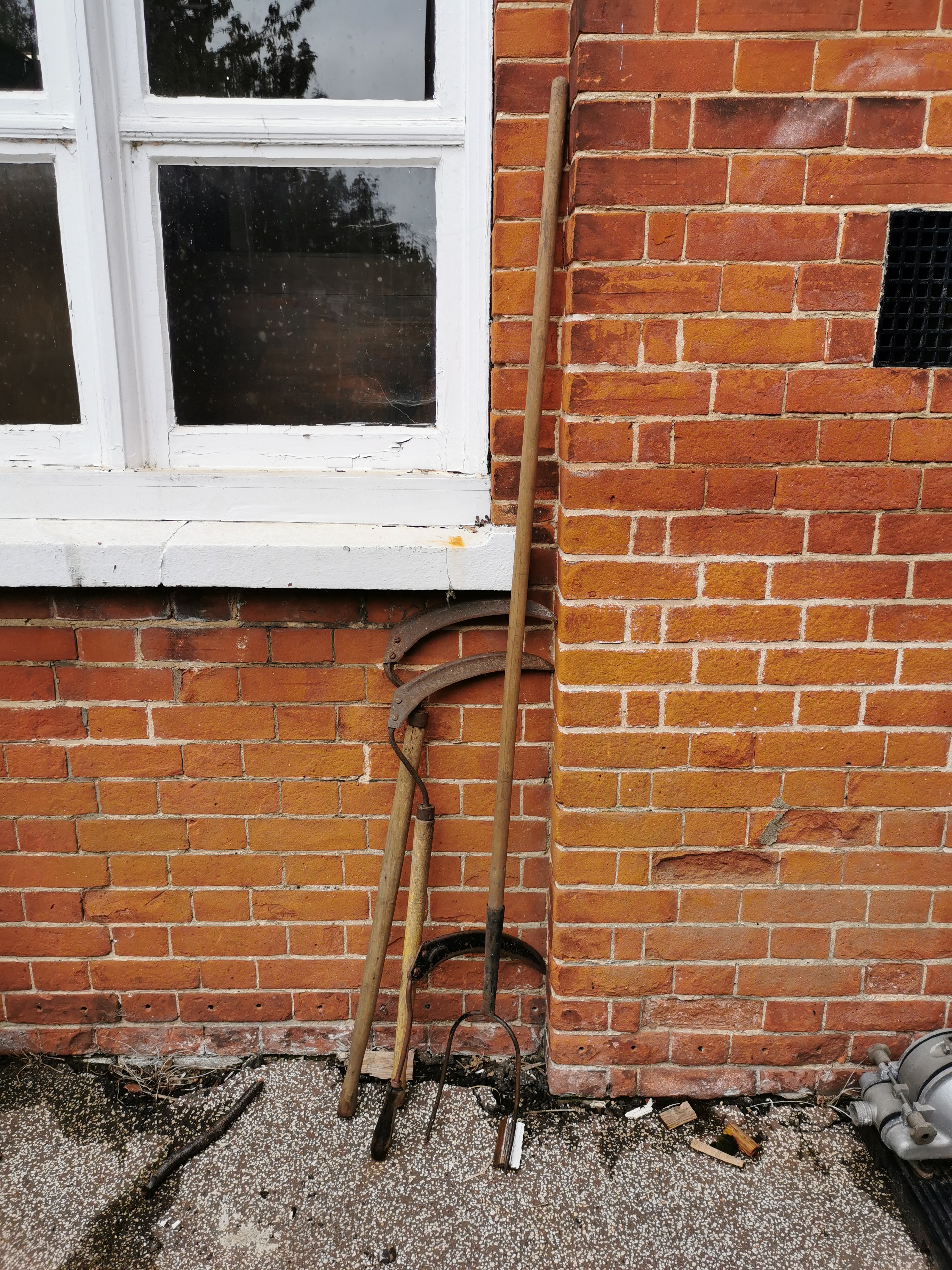 A vintage pitch fork and three vintage scythes of various sizes