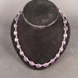 A white metal necklace set with purple coloured stones in closed back setting