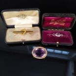 Three yellow metal brooches, one set with large amethyst coloured stone with seed pearl border,