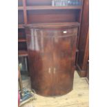 An early 19th Century mahogany bow fronted hanging corner cupboard