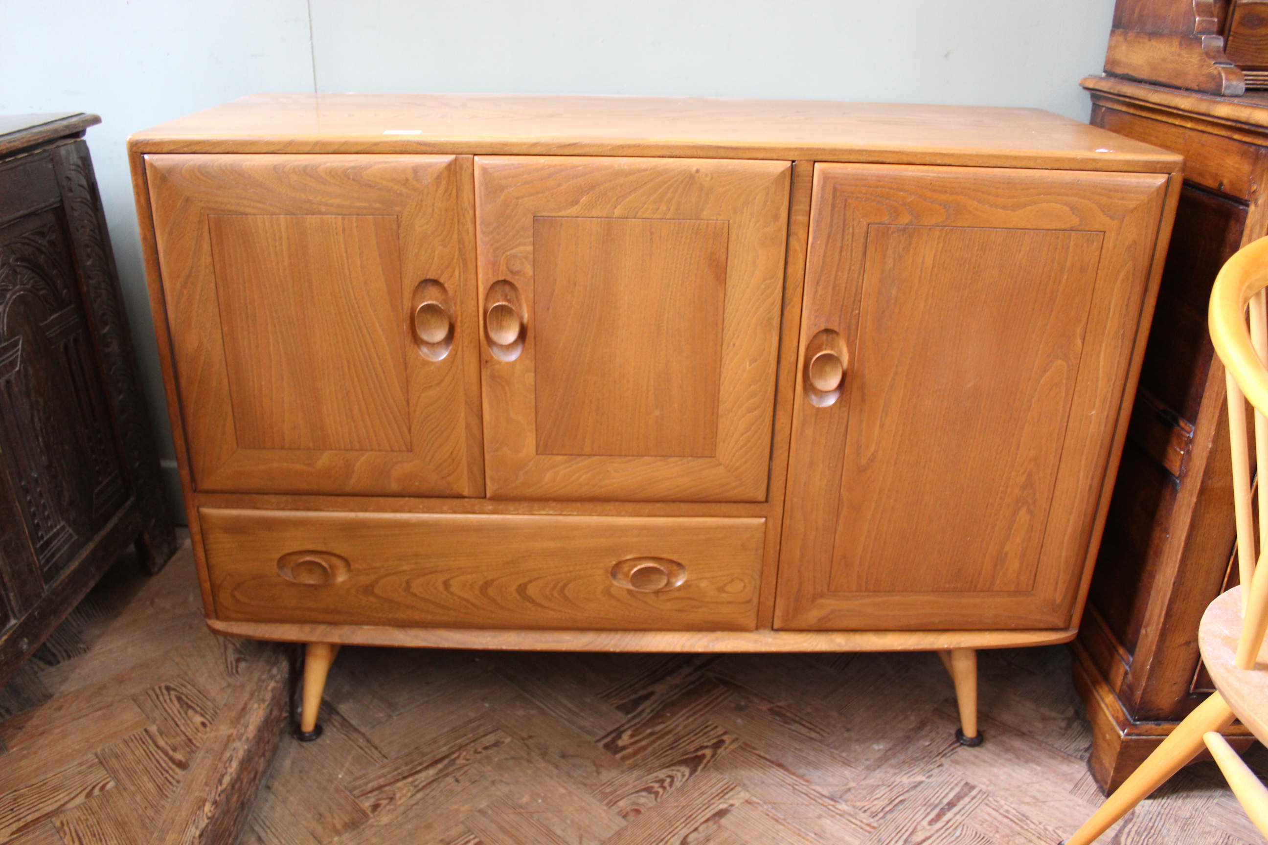 A mid Century Ercol blonde teak sideboard with a combination of three cupboards and a single drawer