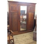 An Edwardian American walnut triple wardrobe with bevelled edge mirror to centre