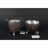 An unusual white metal mounted carved coconut milk jug and sugar bowl, both on three ball feet,