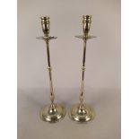 A pair of tall Edwardian brass candlesticks with drip trays, slender stems and circular bases,