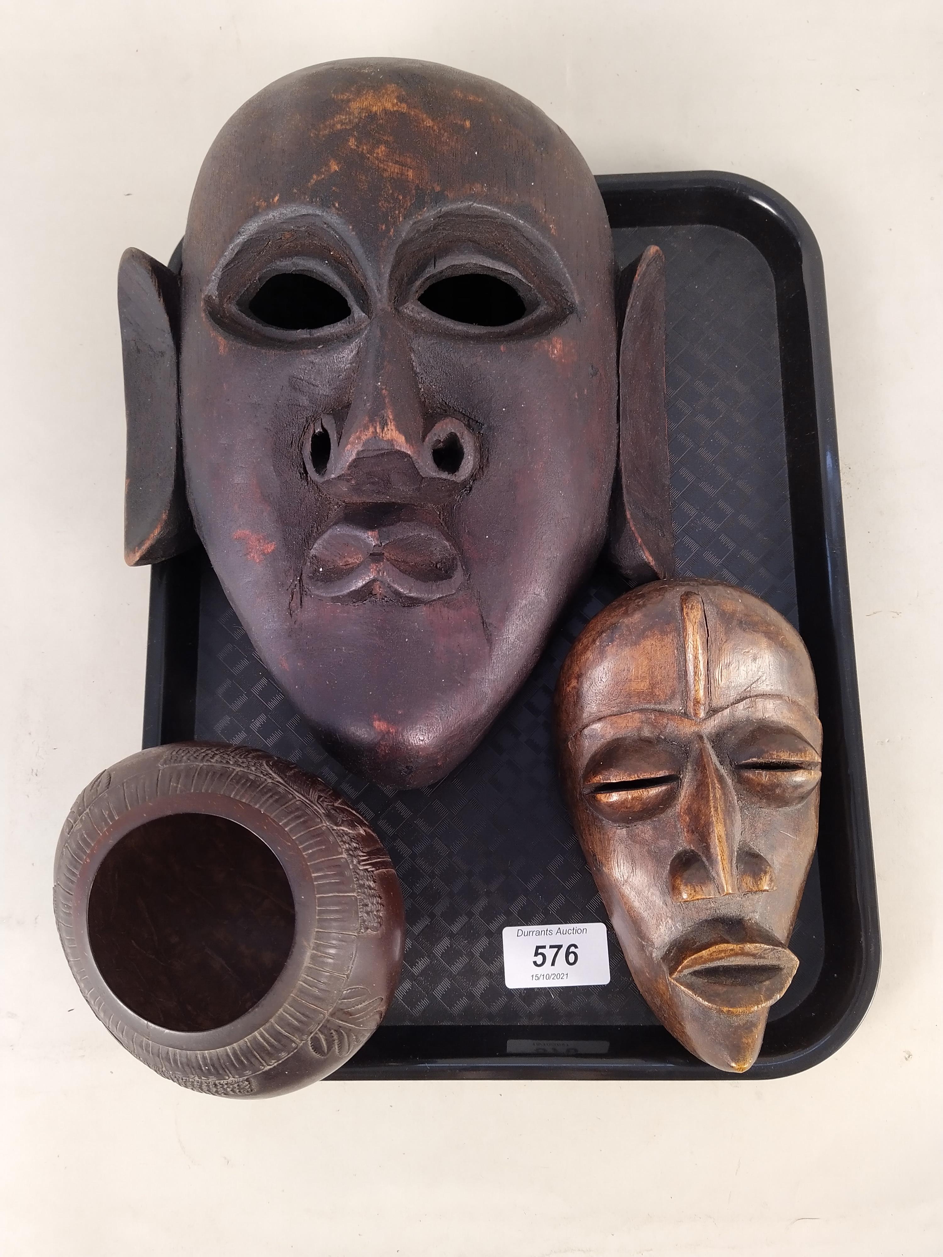 Two African carved wood face masks plus a carved coconut bowl on stand decorated with elephants