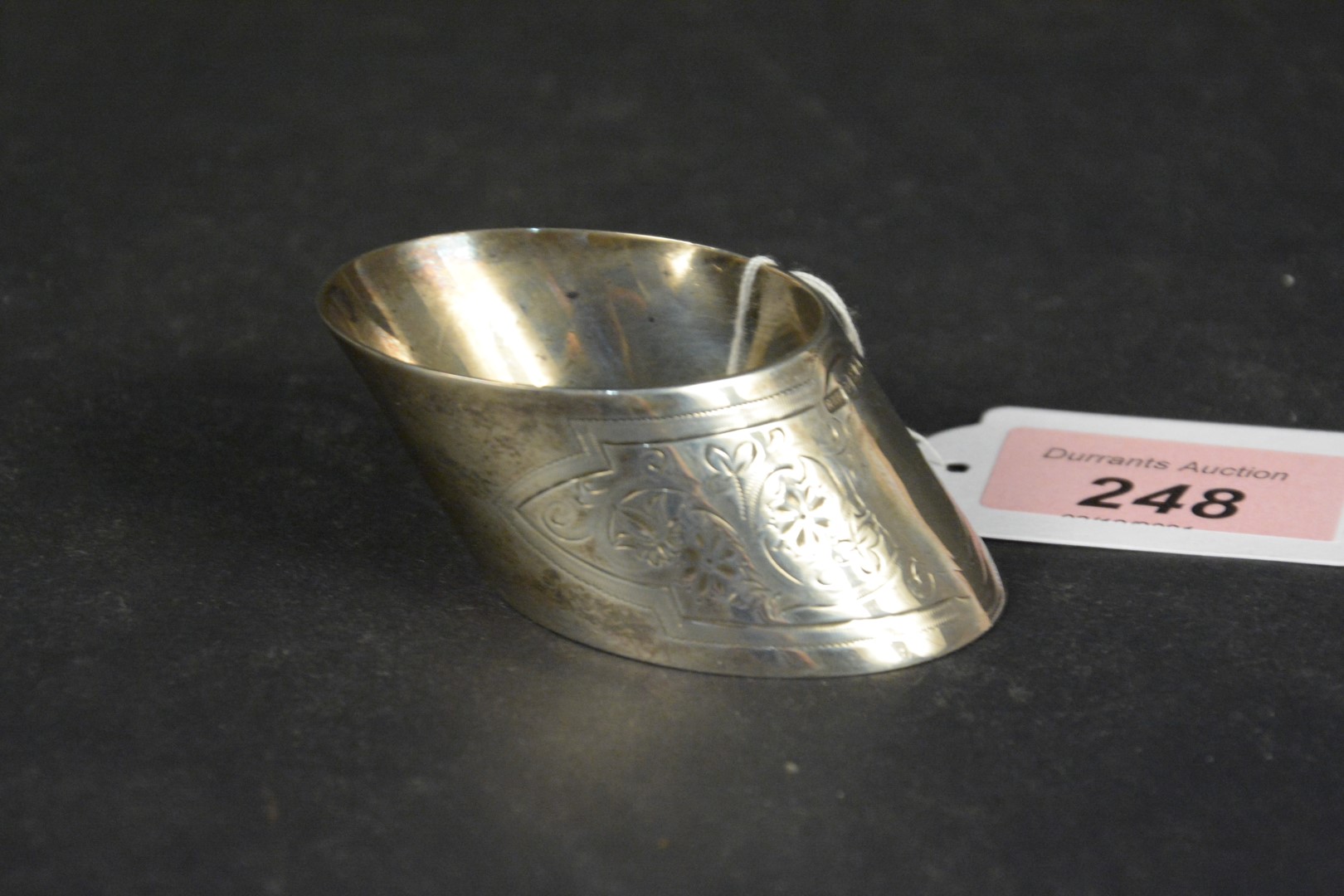 A silver napkin ring of slanted shape with engraved floral decoration, hallmarked Sheffield 1896,