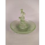 An Art Deco period green glass dish with separate central figures of a boy playing a flute and girl,
