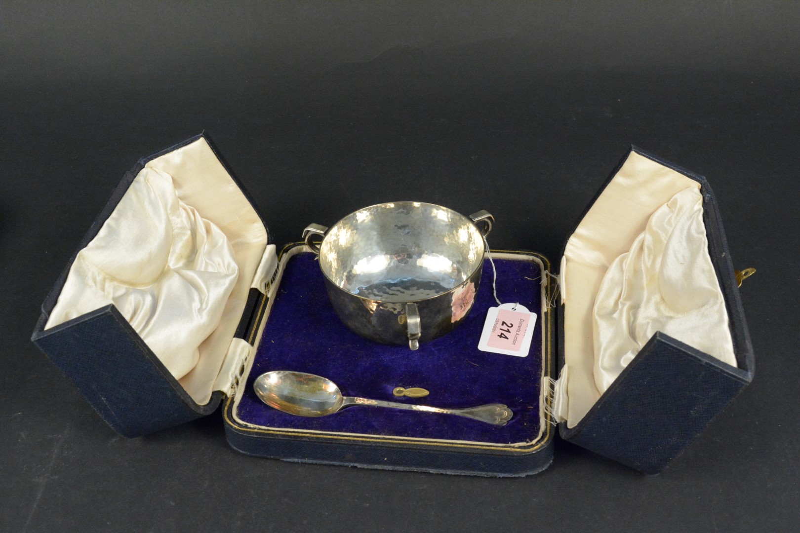 A cased silver three handled bowl and spoon with planished decoration,