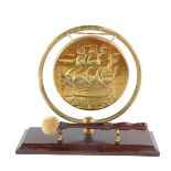 An early 20thC brass table gong, embossed with a galleon, raised on a rectangular oak base with
