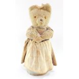 A Reuge musical Teddy bear, wearing a dress and apron, playing rock - a - bye - baby, 36cm high.