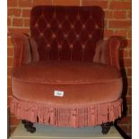A Victorian button back armchair, upholstered in pink draylon, raised on turned feet and castors.