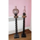 A pair of ebonised open barley twist column lamp standards, housing a clear glass reservoir oil