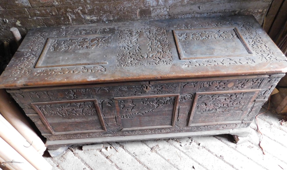 A large 17thC carved poker work walnut coffer, the lid with iron strap hinges and carved figural and