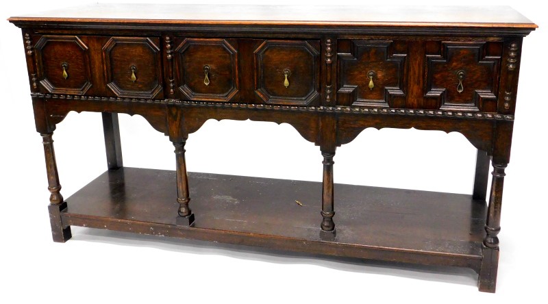 An early 20thC oak dresser base, the top with a moulded edge above three panelled drawers, on turned