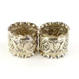 A pair of Edward VII napkin rings, cast with cherubs, scrolls, a vacant cartouche, etc.,