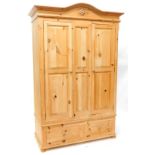A waxed pine double wardrobe, with shaped cornice and two panelled doors, the base with two