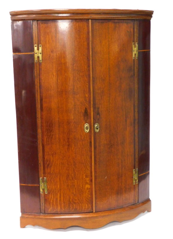 An early 19thC oak and mahogany bow fronted corner cabinet, the doors with H shaped hinges enclosing