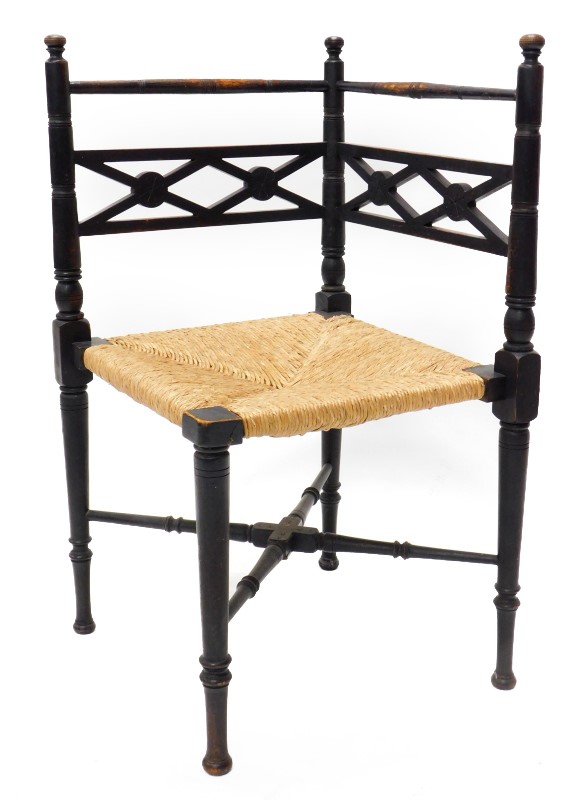 An early 20thC ebonised corner chair, in the aesthetic style, with a rush seat.