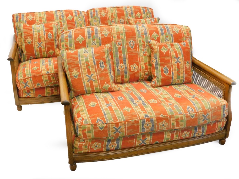 An Ercol elm and caned three seater sofa, and a matching two seat sofa, with geometric multicoloured