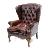 A mahogany wing back chair in George III style, upholstered in red leather on cabriole legs.