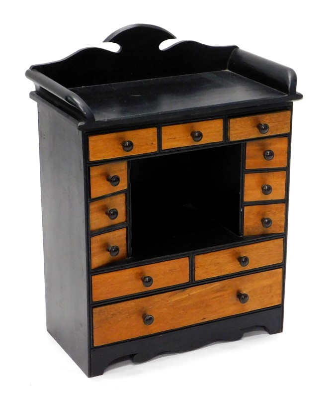 A small ebonised and mahogany table top cabinet, with a raised back and various drawers, each with