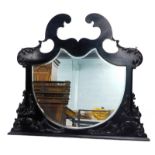 An Edwardian ebonised overmantel mirror, with a cartouche shaped bevel plate surrounded by scroll