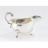 A George V silver sauce boat, with a double C scroll handle, raised on three hoof feet, Birmingham