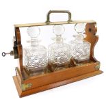 An oak and plated three bottle tantalus, worn, containing cut glass decanters and stoppers, with