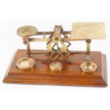 A set of early 20thC brass postal scales, with weights, raised on an oak base, 31.5cm wide.