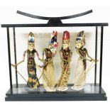 An Eastern glass display case with four puppet figures, each in floral dress with sequin
