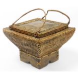 An Eastern wicker storage basket, shaped rectangular form, on a wooden base, with two carrying