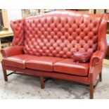 A Chesterfield style three seater chair, the red button back upholstery, on a mahogany base, 130cm